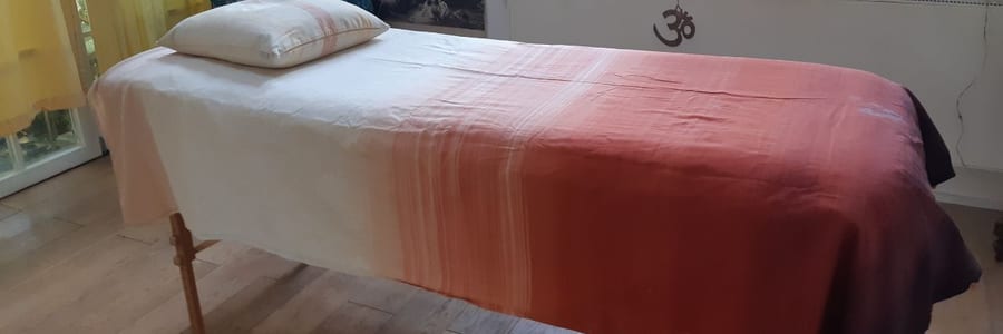 Behandlungsliege mit rot getöntem Tuch in einem hellen Raum mit Pflanzen am Fenster