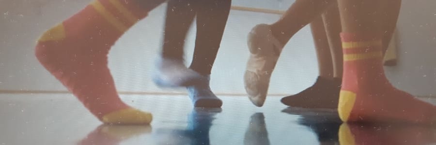Kinderfüße in bunten Ringelsocken und Ballettschläppchen tanzen auf einem spiegelnden Hallenboden