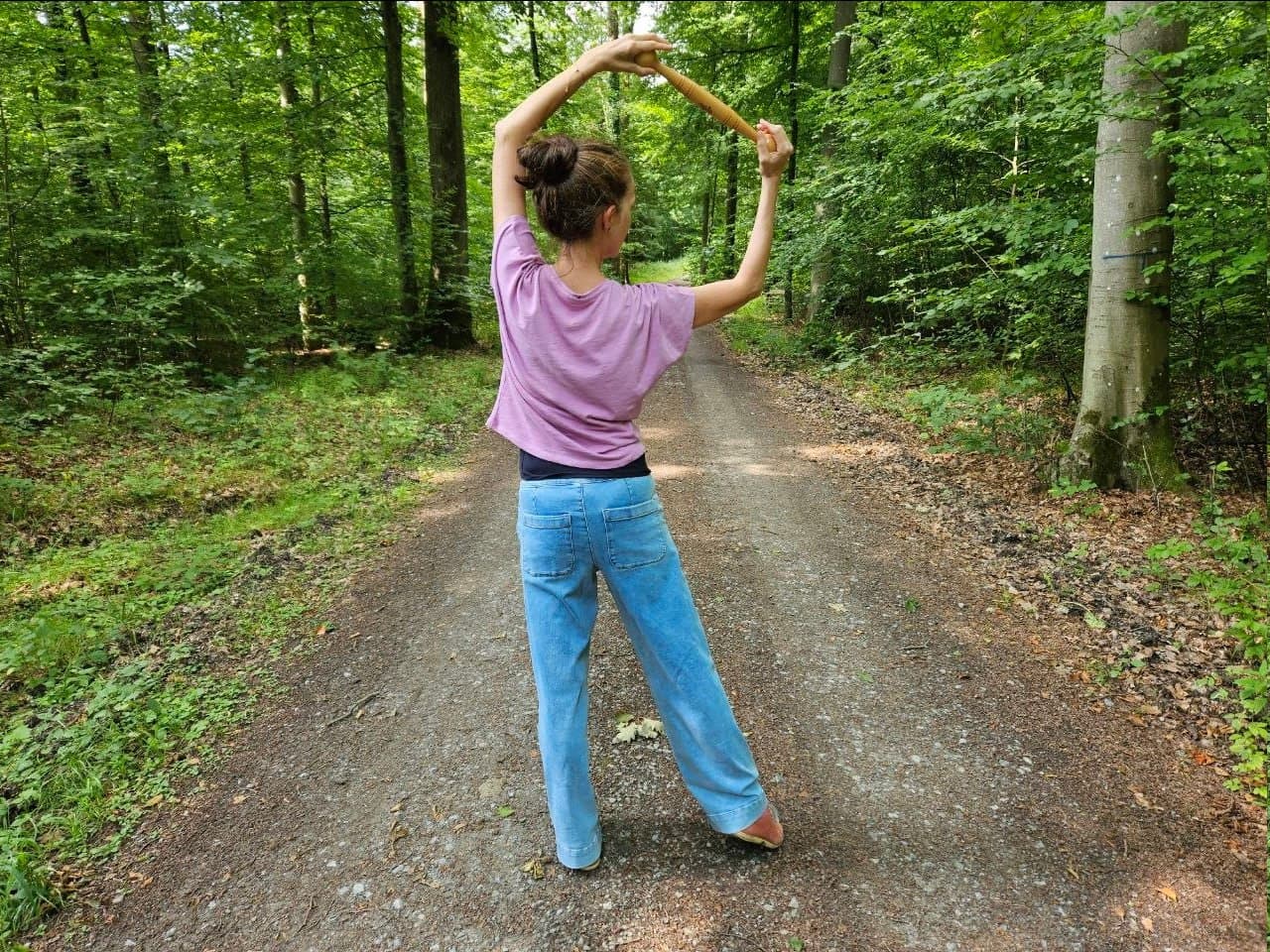 Sylke steht auf einem Waldweg, den Idogostab mit beiden Händen über dem Kopf