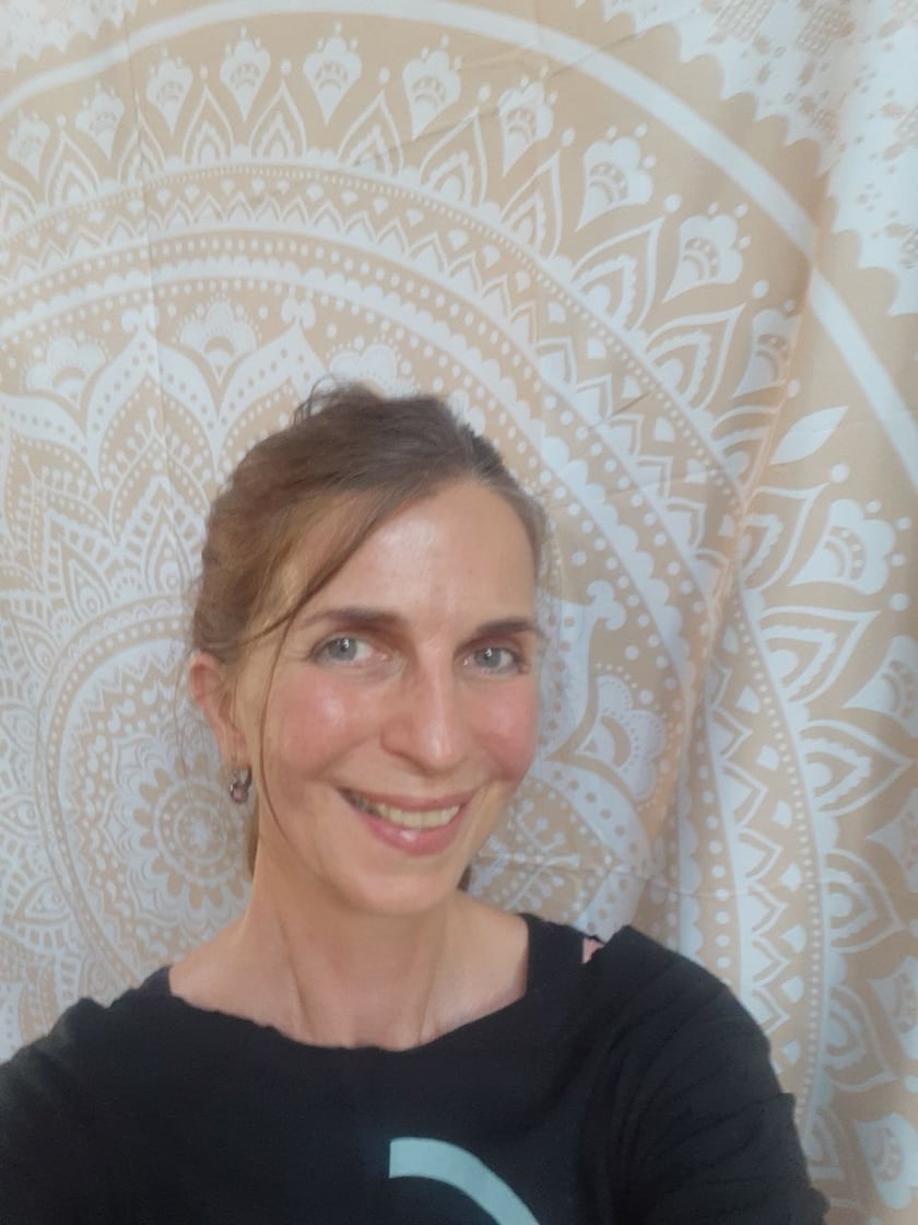 Sylke lächelt in die Kamera, im Hintergrund ein Tuch mit Mandalamuster