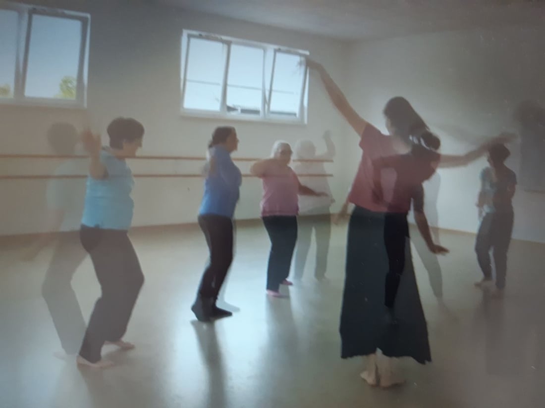 Eine Gruppe Erwachsener tanzt barfuß in einem hellen Saal mit Ballettstangen