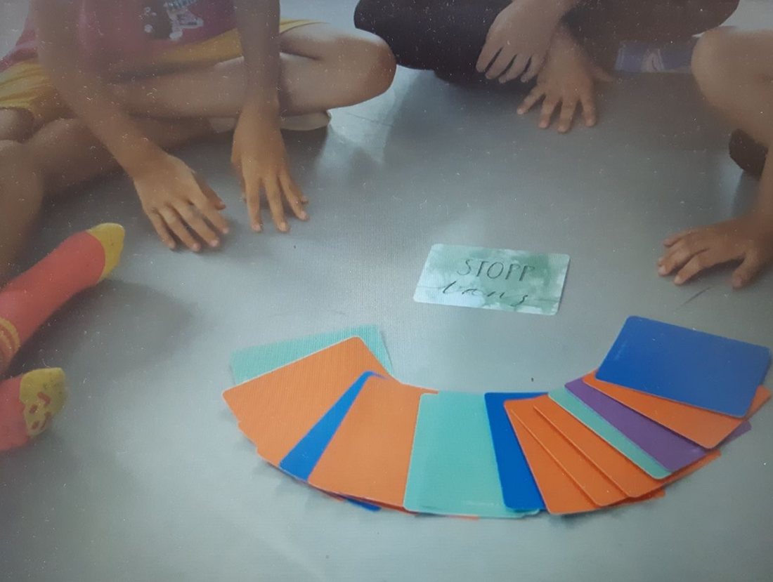 Kinder sitzen im Kreis um aufgefächerte bunte TanzSpielKarten und eine Stopp-Karte