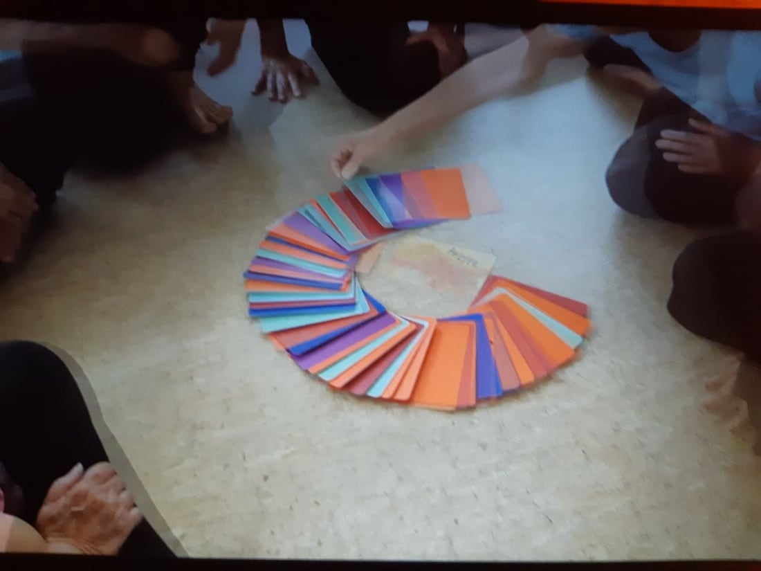 Die TanzSpielKarten liegen als bunte Spirale auf dem Boden, Hände legen weitere Karten an